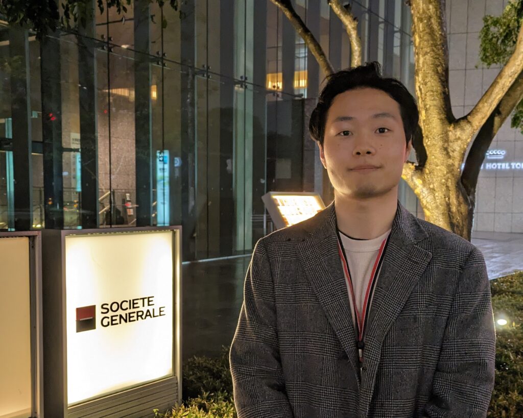 iCLA graduate Takaaki stands in front of his workplace.