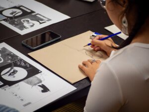 An iCLA student sketches upside down on a piece of paper, drawing the haiku picture next to her.