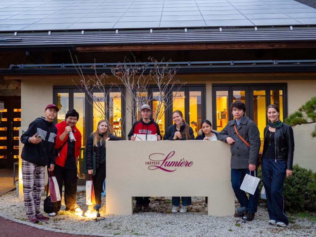 iCLA students stand around Lumiere Winery's sign, where they learned about wine making in Yamanashi.