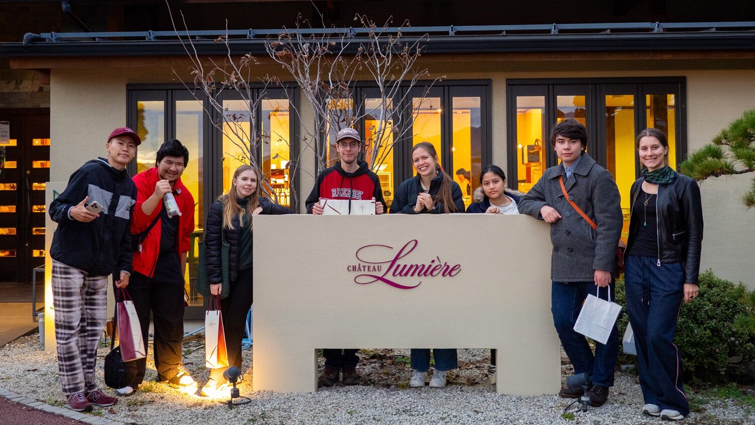 iCLA students stand around Lumiere Winery's sign, where they learned about wine making in Yamanashi.