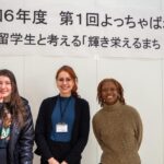 iCLA International Students and the Coordinator of International Relations at the Kofu City Hall stand together under the sign with the title of the roundtable discussion.